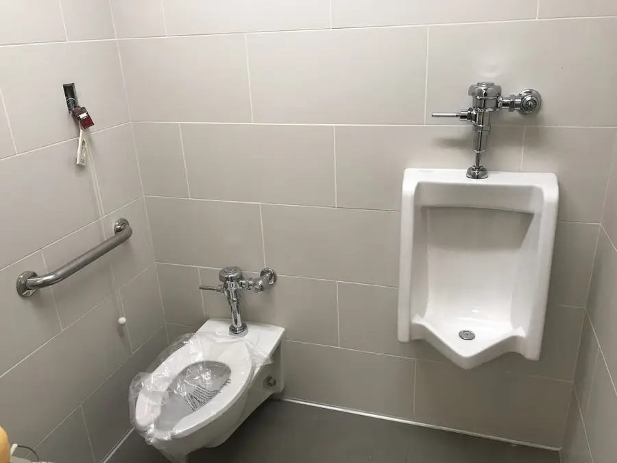 Finished commercial restroom with a tiled wall, grab bar, floor-mounted toilet and wall-hung urinal