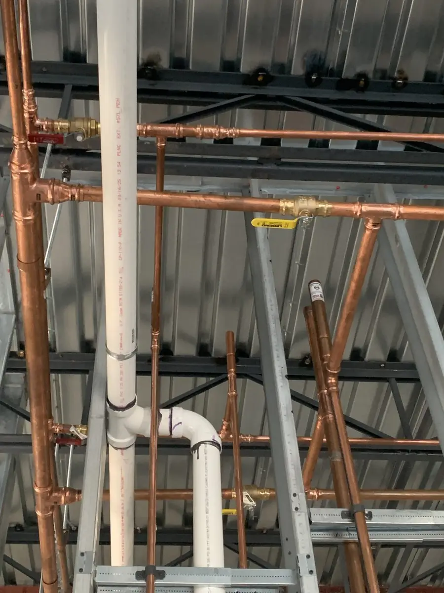 Copper and PVC risers roughed in through a commercial stud wall with the pipe supports strapped off