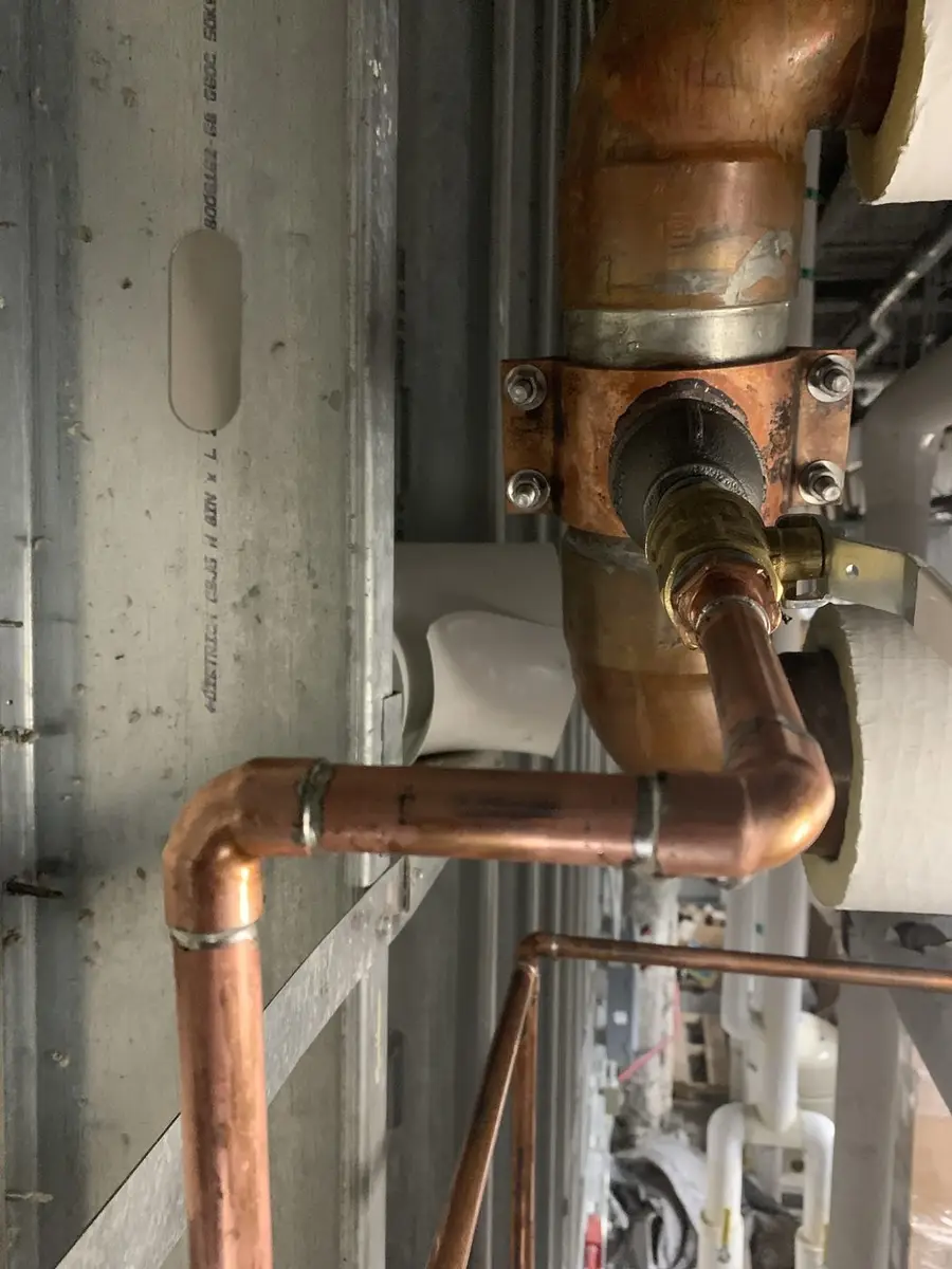 Close detail of soldered copper fittings and a brass valve body on a finished riser