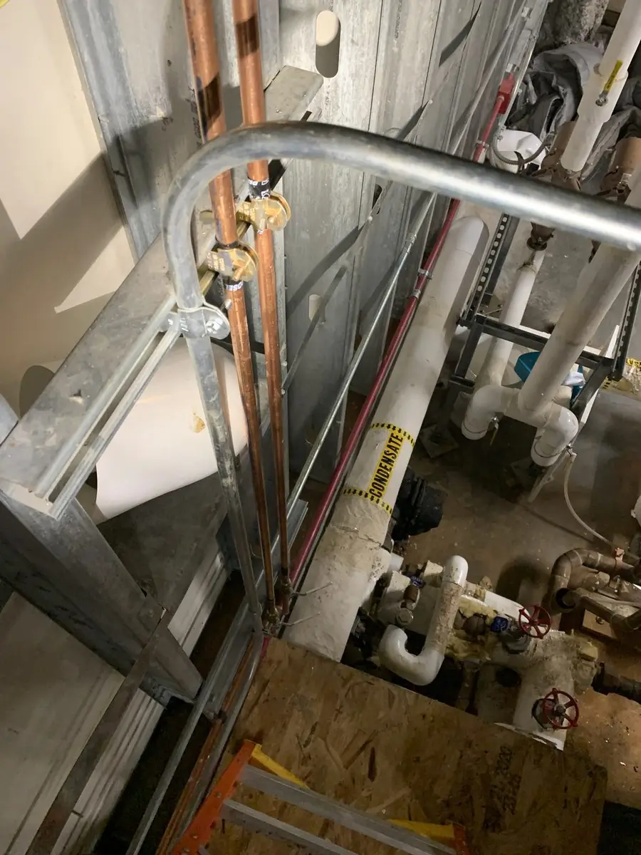 Copper main riser run vertically through a commercial pipe chase alongside insulated ductwork