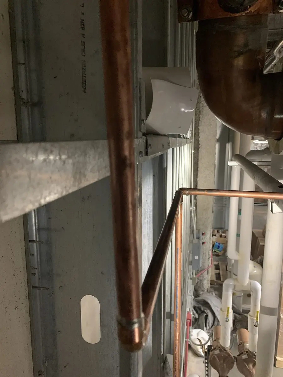 Soldered copper tee assembly clamped to a wall with the branch lines squared off