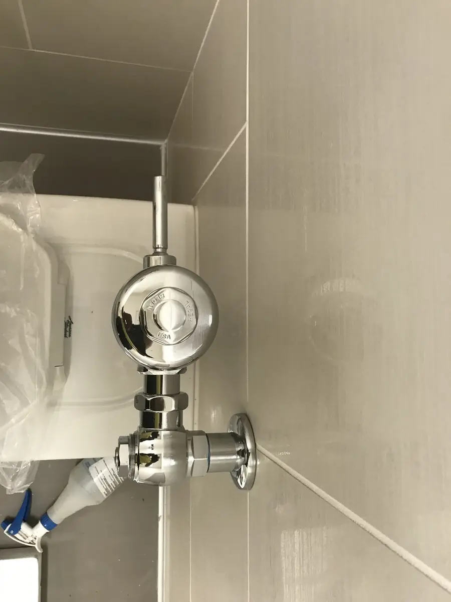 Chrome flushometer valve installed on a new fixture still in its factory wrapping
