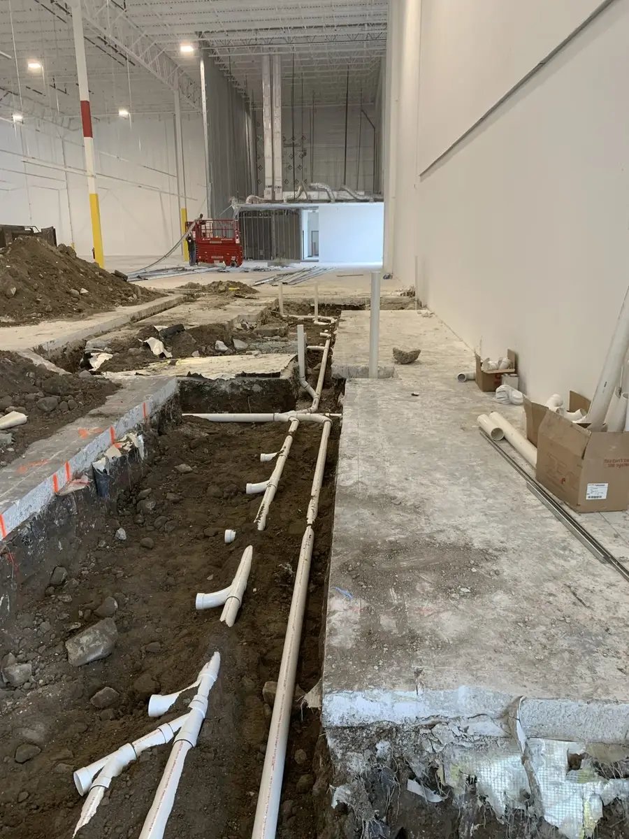 PVC drain line laid in an open trench cut through the slab of a commercial interior