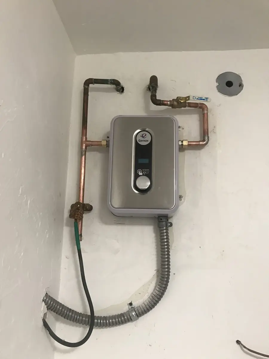 Compact point-of-use water heater mounted on a wall with copper supply lines and a flexible conduit