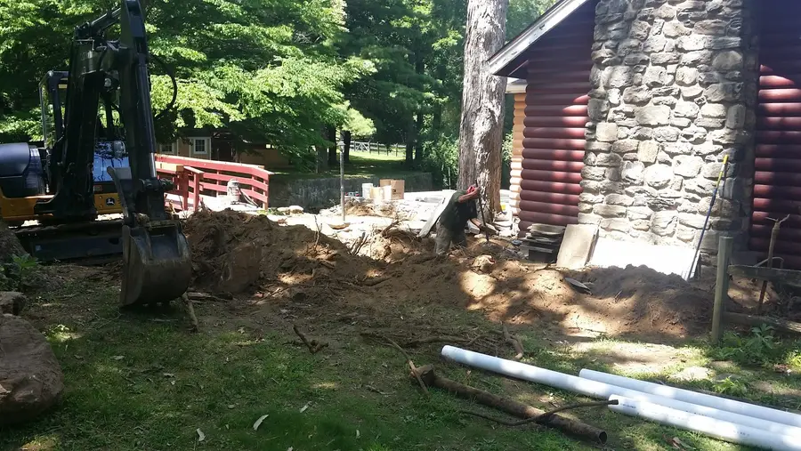 Excavator working alongside a house with lengths of new pipe laid out ready to go in the trench