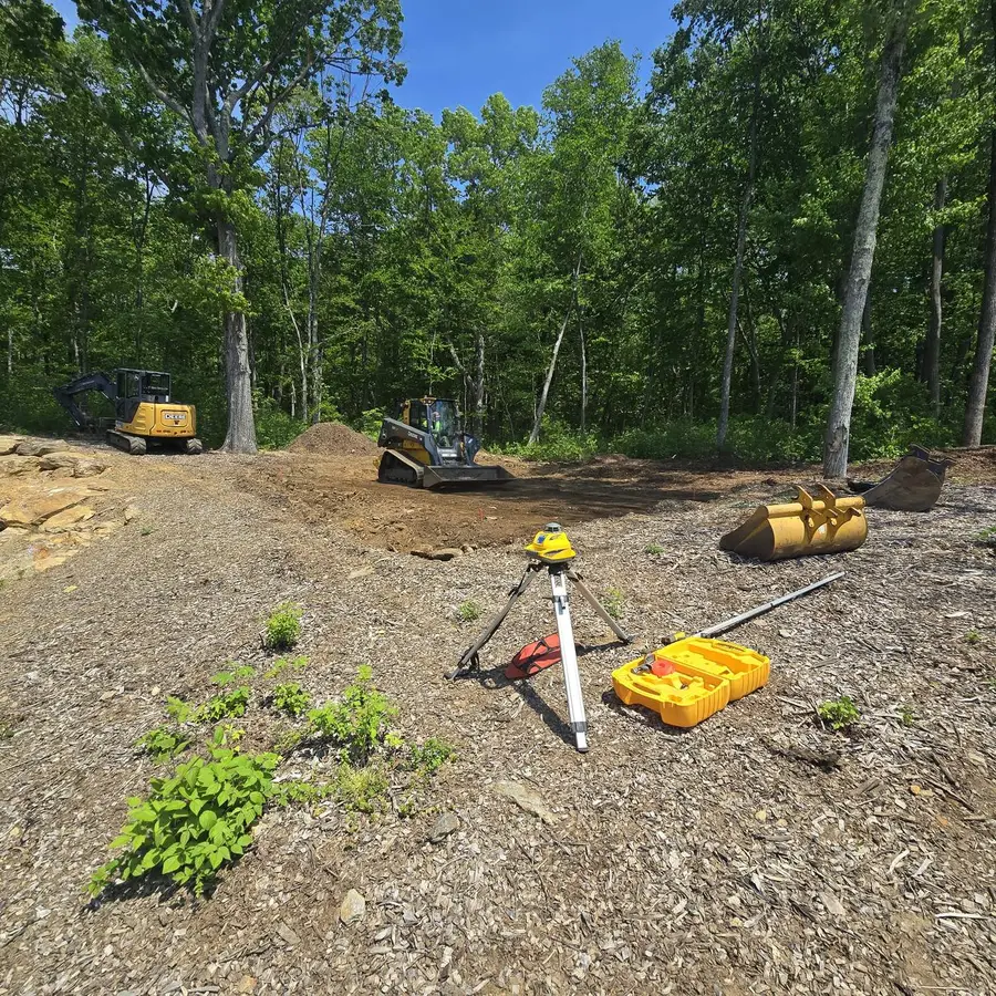 Cleared building site with a surveying tripod set up and excavators positioned for utility trenching