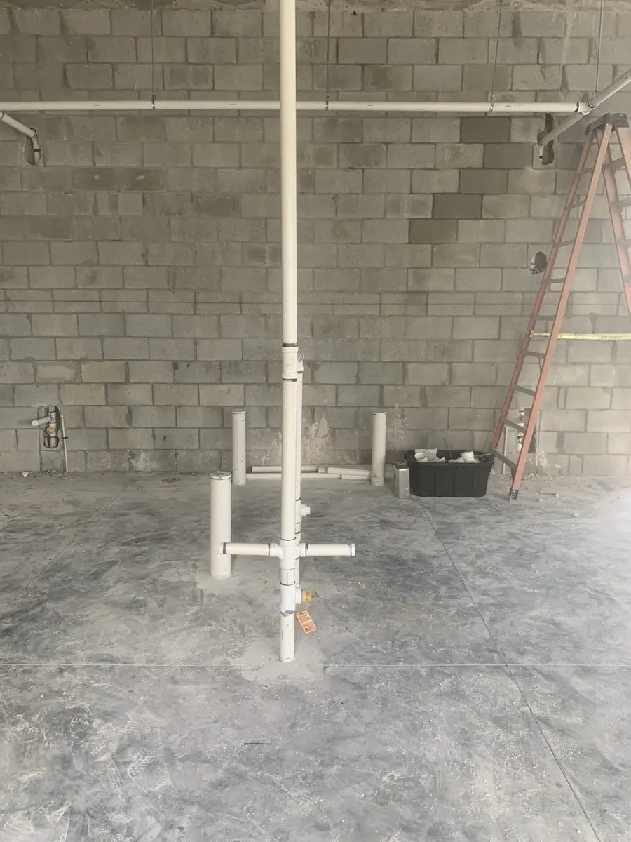 PVC waste and vent stub-ups standing out of a finished concrete slab against a block wall
