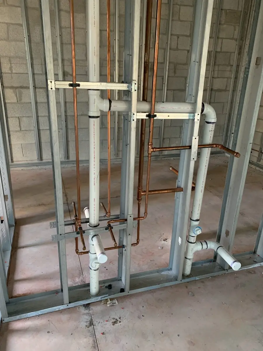 Copper water lines and PVC drain and vent stacks roughed into metal stud walls before drywall