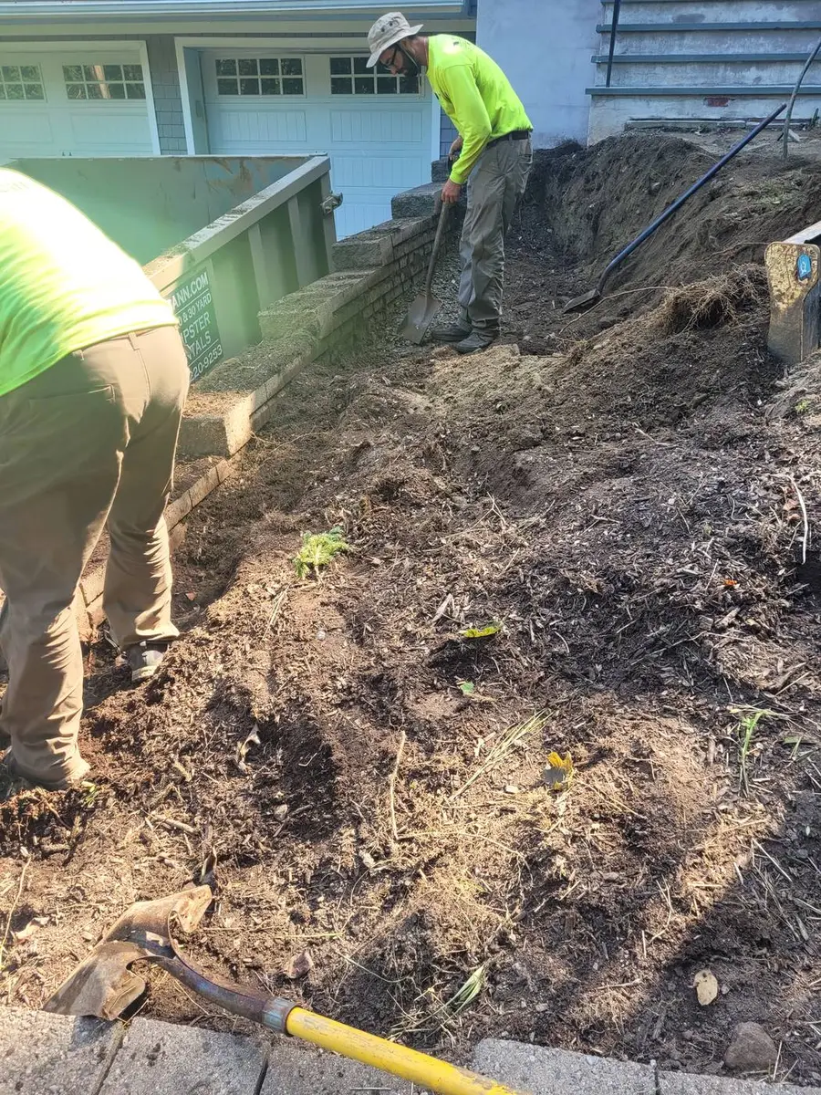 Two crew members in high-visibility shirts hand-digging to expose an underground line beside a building