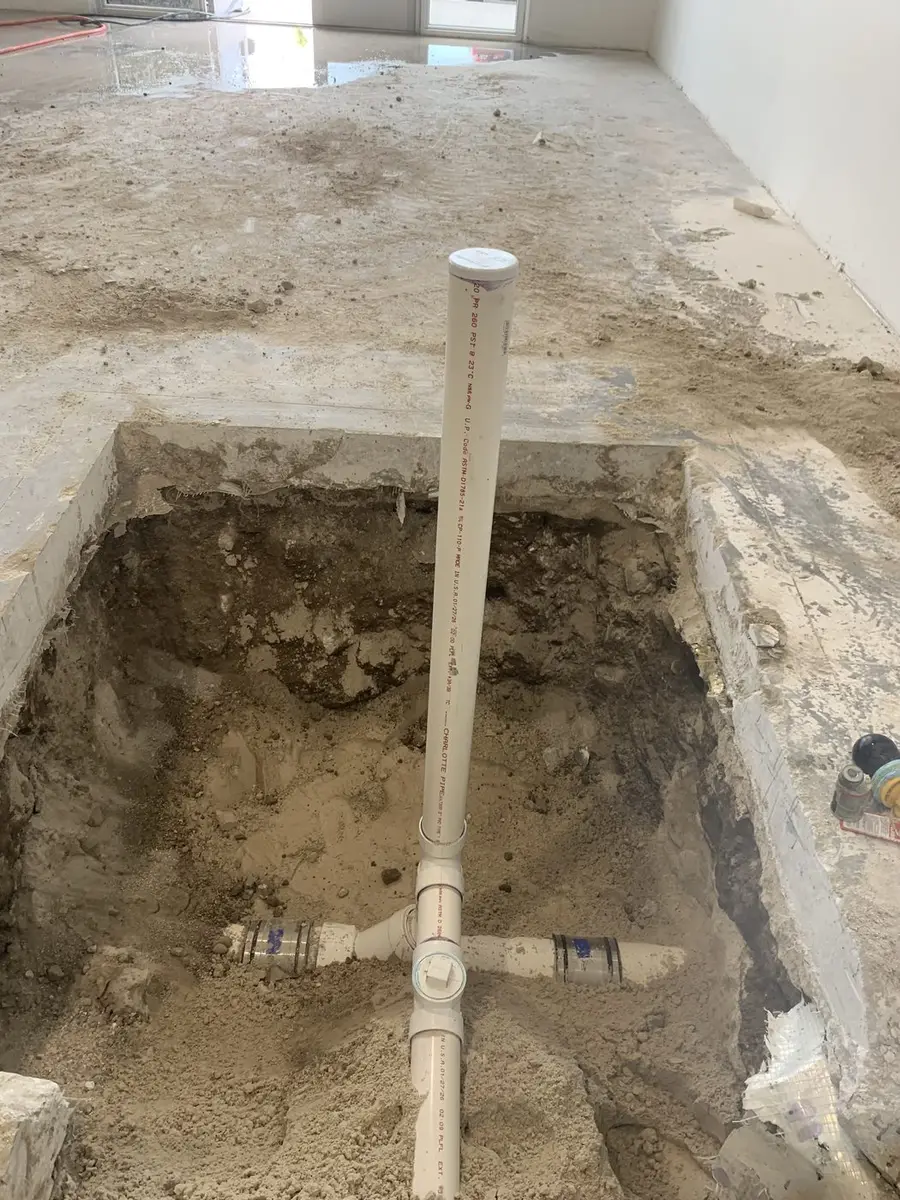 Excavated pit exposing a PVC cleanout and combination fitting on an under-slab drain line