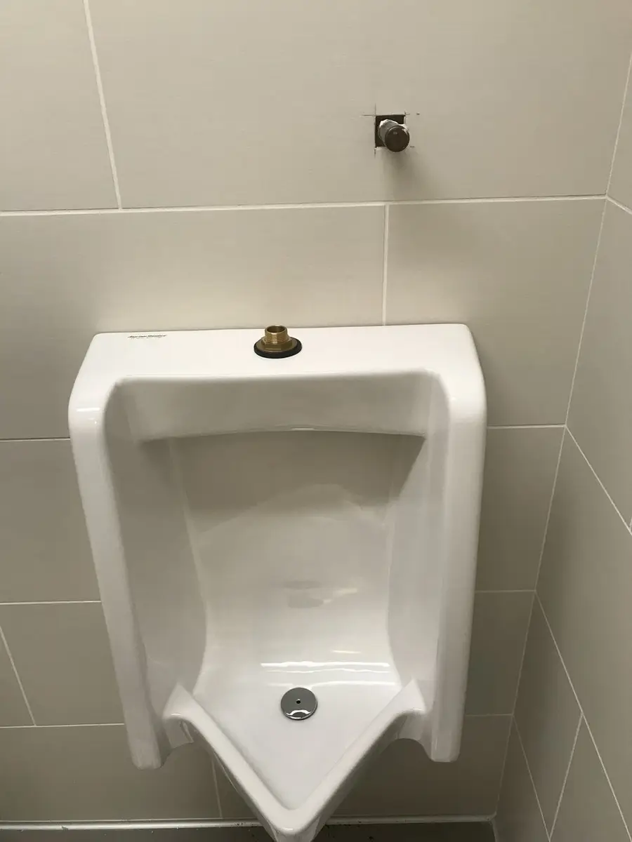 Wall-hung urinal set on a tiled wall with the flush connection roughed in above it